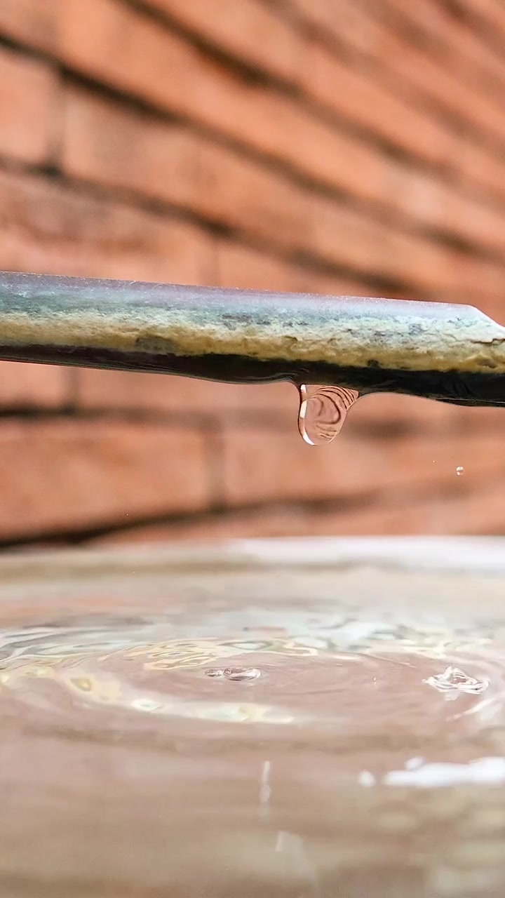 Goccioline d'acqua al rallentatore cadono da un tubo creando increspature in un lavabo su uno sfondo di mattoni
