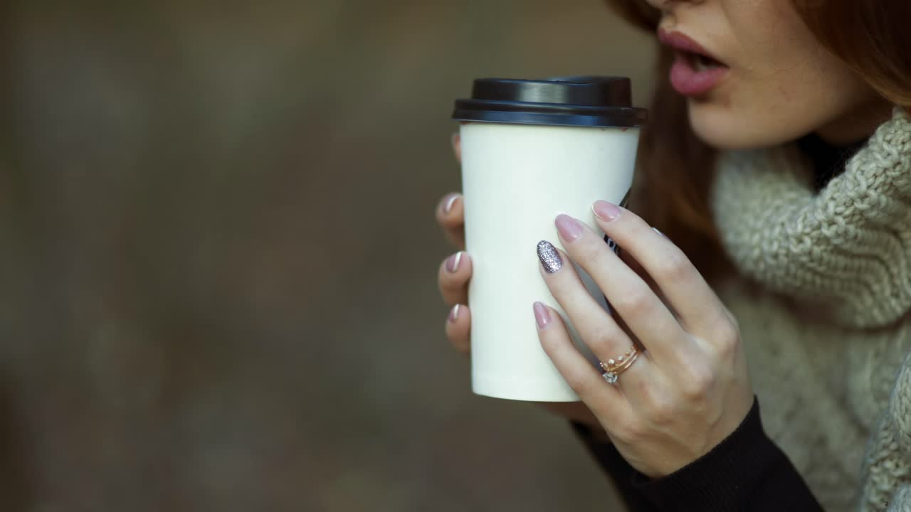 Girl drinking coffee in park. Young woman holding cup of coffee in the autumn forest