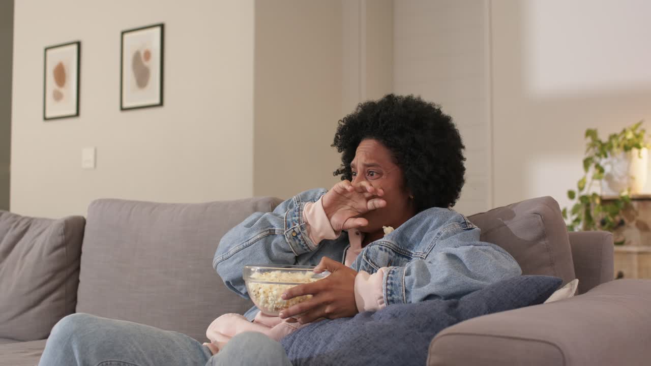 Donna che guarda un programma, prende popcorn dal divano mentre un movimento fa rovesciare i popcorn, si asciuga le lacrime