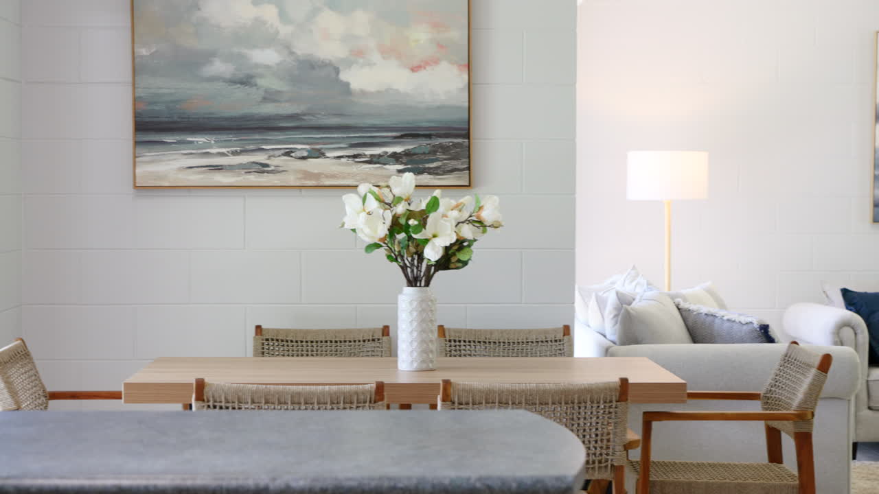 pan a través de sillas tejidas de ratán y sofá de color azul blanco neutral sala de estar con pinturas abstractas de temas de nubes de agua del océano