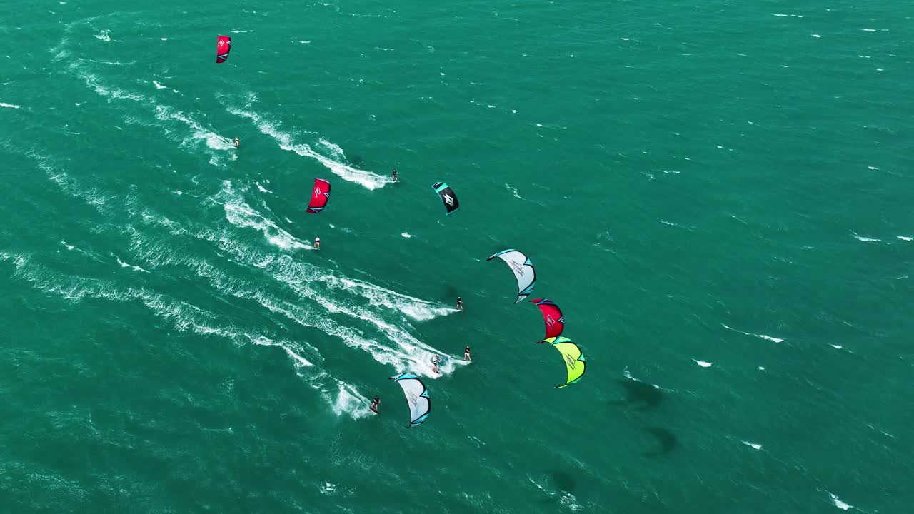 여름에 바다 위를 질주하는 다채로운 연과 카이트 서퍼 그룹을 보여주는 공중 하향식