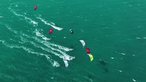 aerial top down showing group of colorful kites and kite surfer speeding over ocean in summer