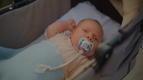close up of baby sucking pacifier in stroller at sunset