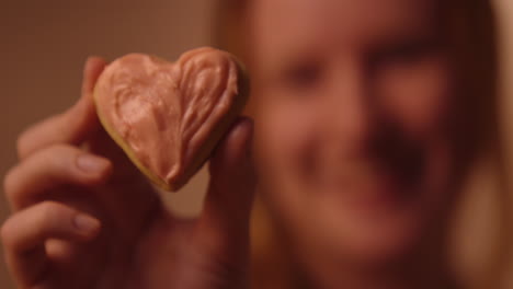 smiling woman holding a heart-shaped cookie