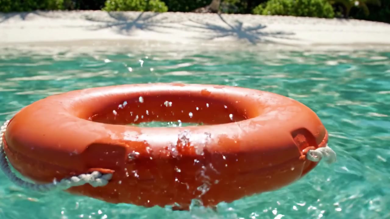 An Orange Lifebuoy Floating Gracefully in Crystal Clear Water with a Sandy Beach and Lush Greenery in the Background, Perfect for Summer Safety and Fun.