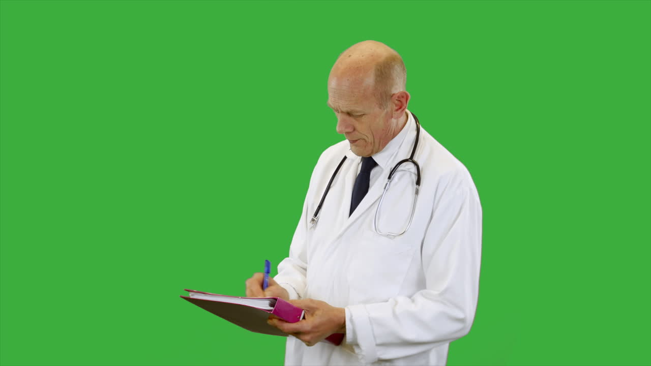 Side view of a doctor wearing a scientist white lab coat is listening and taking notes on a clip board. The man is wearing a shirt and tie with stethoscope.