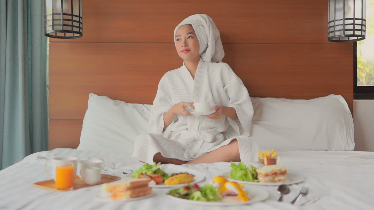 Young woman in bathrobe enjoying breakfast in bed. Slow motion