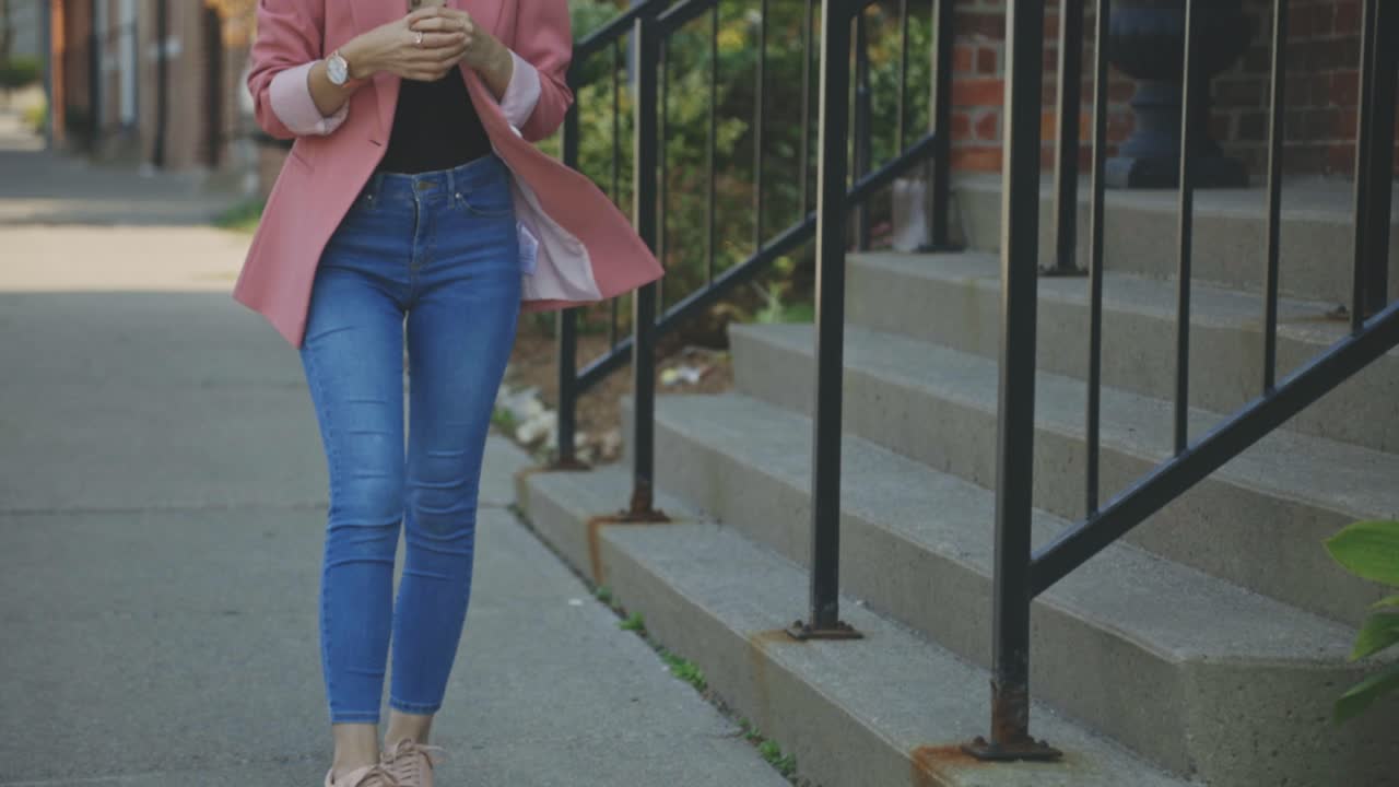 Cropped Image Of A Female Model Dressed In Blue Jeans And Pink Single-Button Blazer Standing Outside The Building - Slow Motion