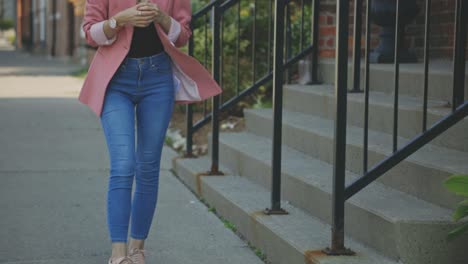 cropped image of a female model dressed in blue jeans and pink single-button blazer standing outside the building - slow motion