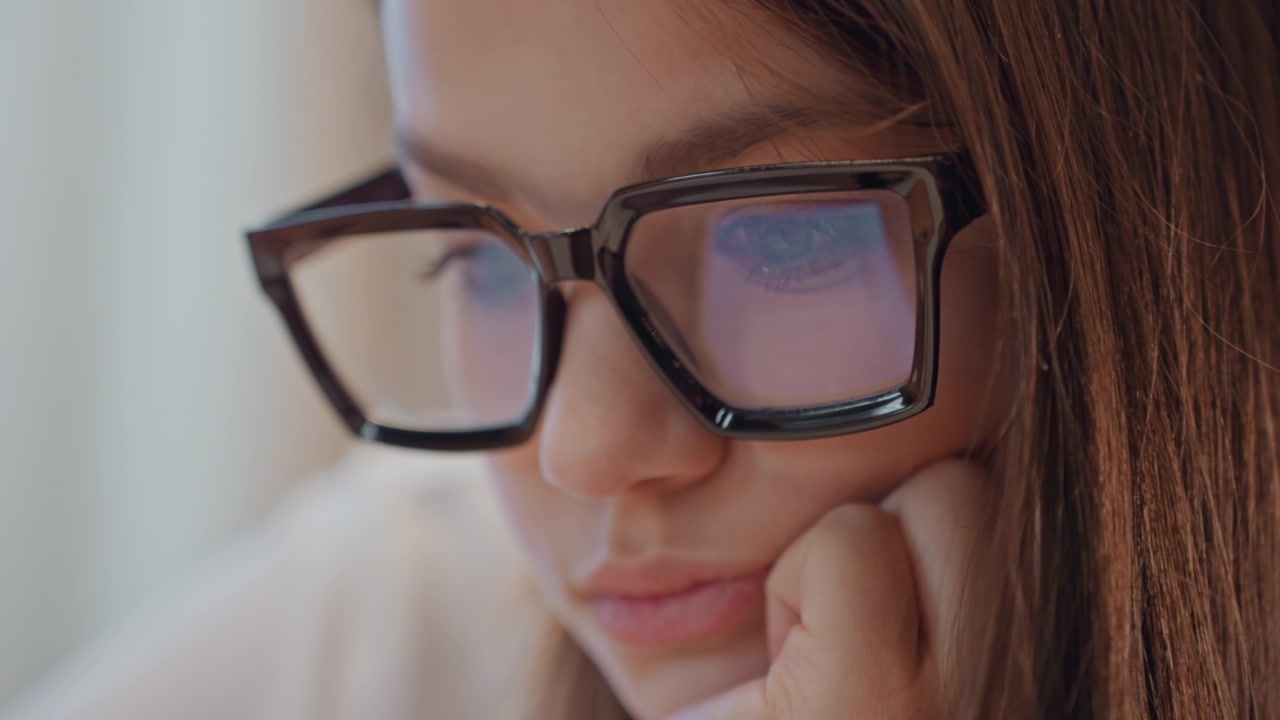 Woman with glasses analyzing screen. Woman wearing spectacles reviewing code during daylight hours. Female developer concentrating on computer screen while working remotely in bright sunlight