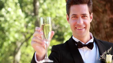 happy groom smiling at camera and toasting with champagne