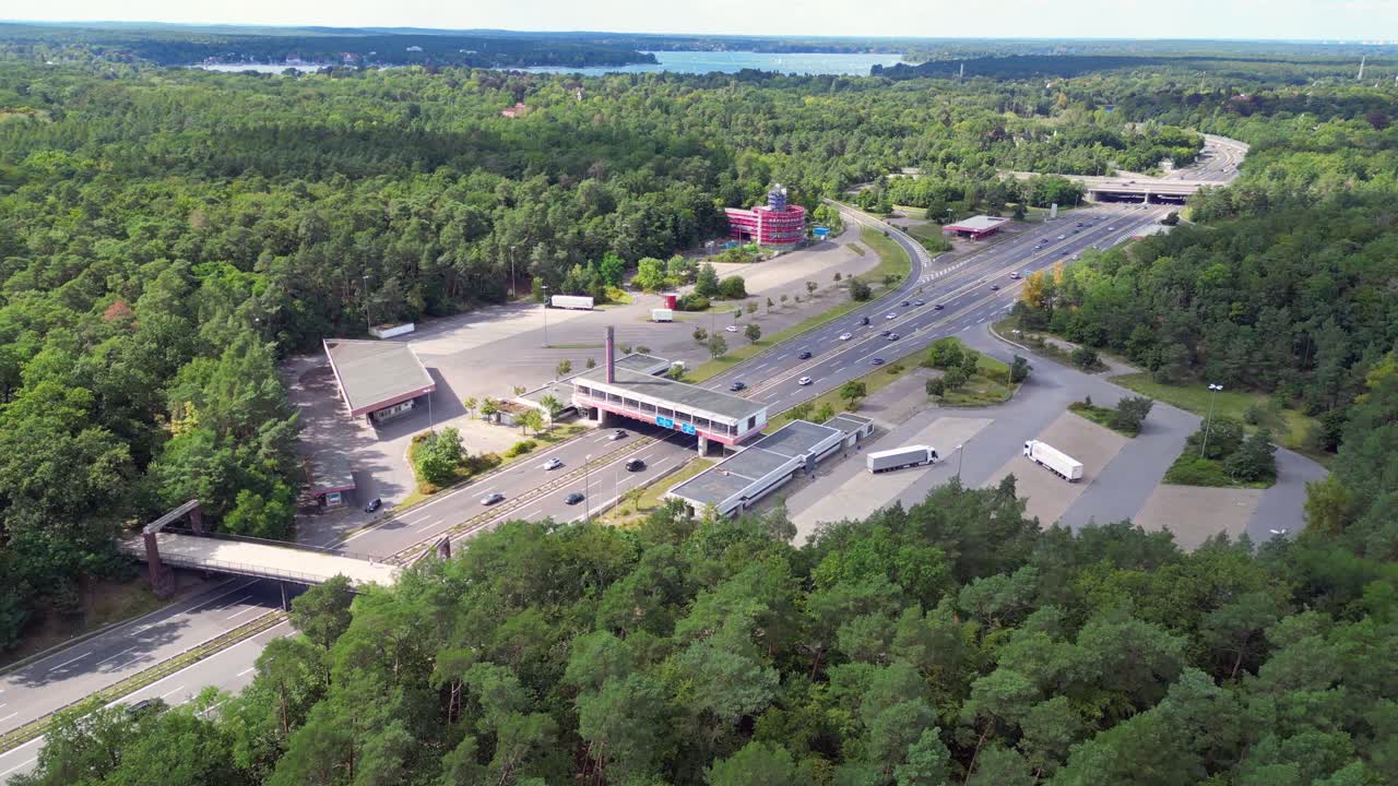 Cars driving on a freeway interchange surrounded by forest leading to a lake on a cloudy day. Marvelous aerial view flight speed ramp hyper motion time lapse