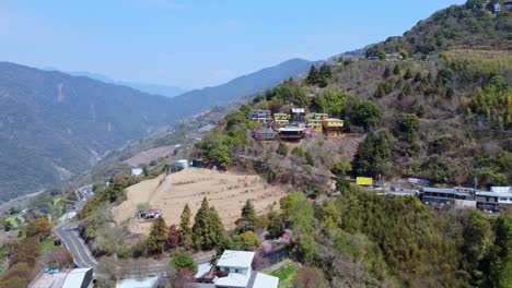 A-colorful-monastery-nestled-in-lush-green-mountainside,-serene-and-remote,-aerial-view