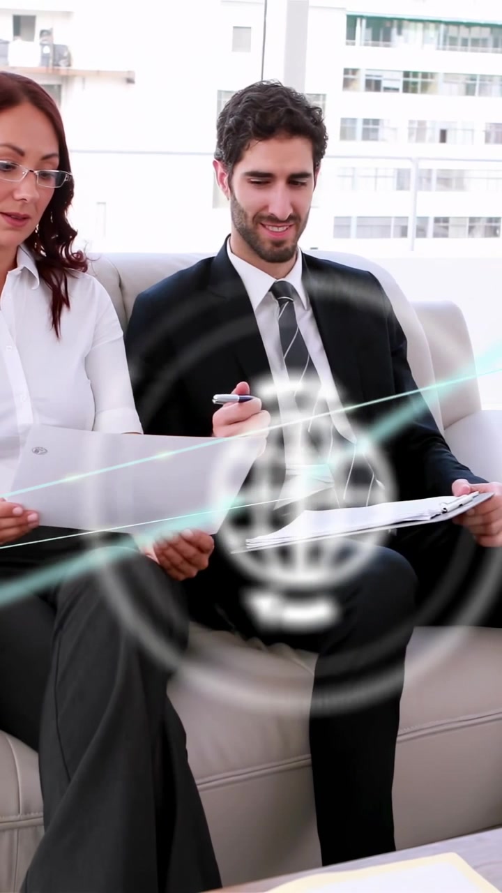 Video vertical: Dos profesionales de negocios en un sofá revisando documentos, hombre tomando notas, generando gráficos HUD sobre los documentos.