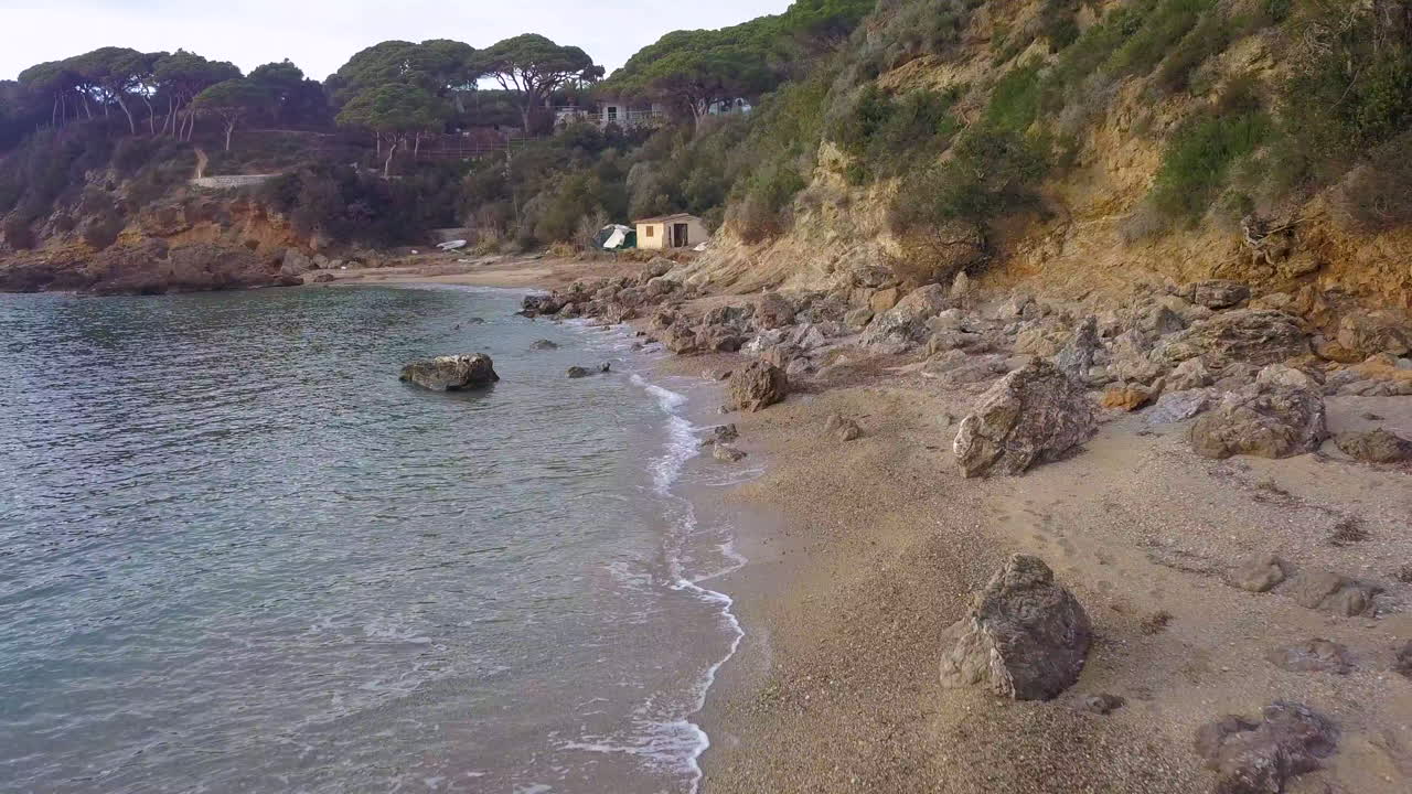 Ripresa aerea con drone che vola lungo la Spiaggia di Zuccale e le scogliere costiere all'Isola d'Elba, Italia, al tramonto