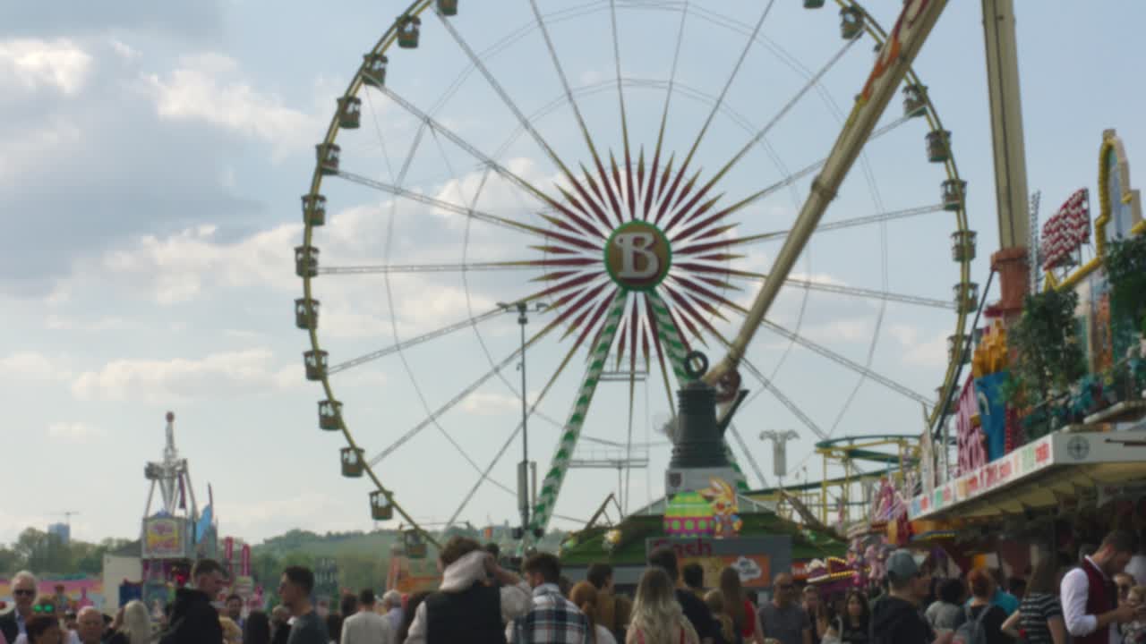 Crowds of people walking towards large ferris wheel at Balvarian outdoor Spring Fest in Stuttgart, Baden Wurttemberg, Germany, Europe, afternoon panning view angle