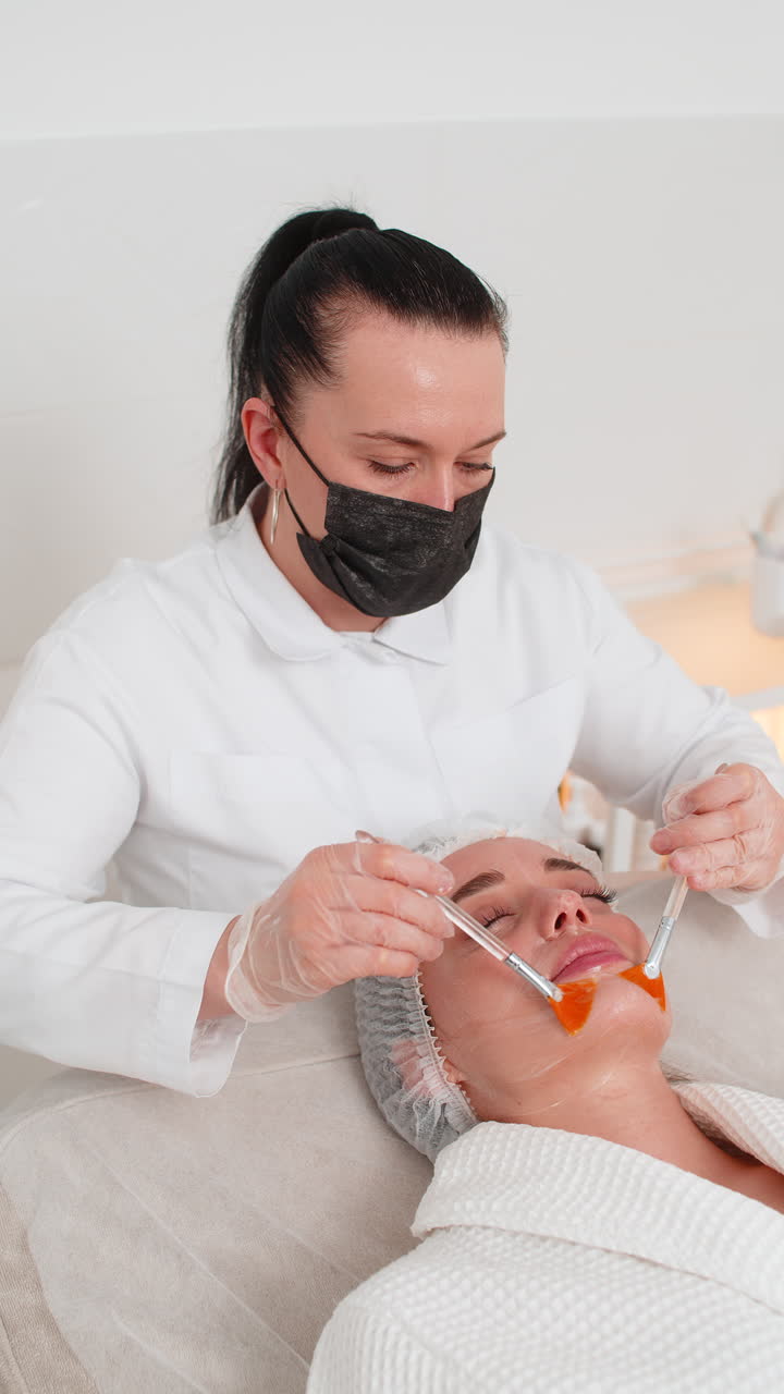 terapia enzimática esteticista aplicando crema médica hidratante en la cara de una mujer joven adulta con pinceles