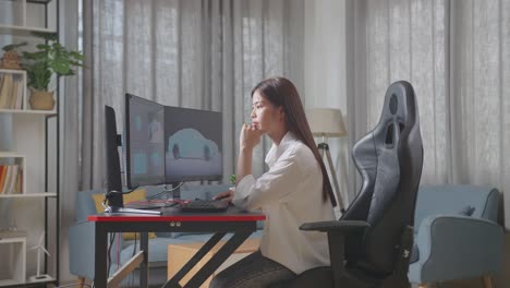 side view of asian female automotive designer thinking of idea while working on 3d model of ev car on the desktop computers in the studio