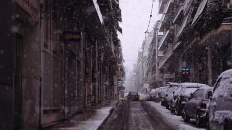 Toma-Urbana-Cinematográfica-En-Cámara-Lenta-De-Un-Automóvil-En-Una-Carretera-Mientras-Nieva-En-El-Centro-De-Atenas,-Copos-De-Nieve-Por-Todas-Partes