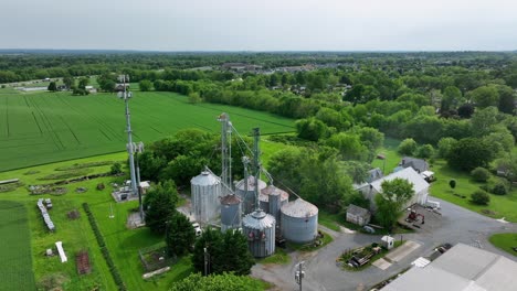aerial view of a rural american farm with silos, barns and lush green fields. classic countryside scene showcasing agriculture and farming infrastructure. aerial approaching shot.
