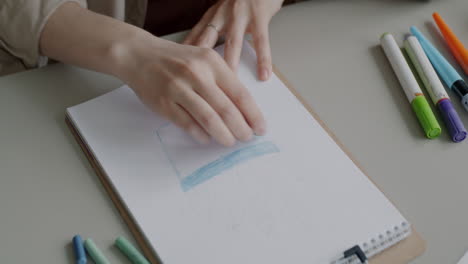 Person sketching with colored pencils and markers on sketchpad.