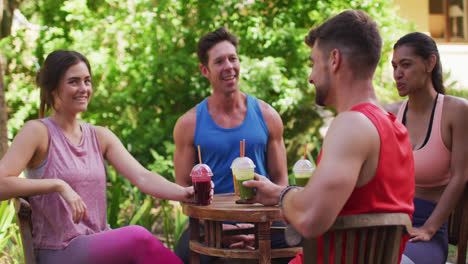 smiling diverse group sitting at table with health drinks, talking after yoga in sunny park