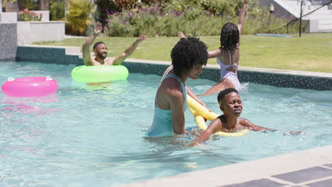 Feliz-Madre-Afroamericana-Enseñando-A-Su-Hijo-A-Nadar-Con-Fideos-Flotando-En-Una-Piscina-Soleada,-Cámara-Lenta