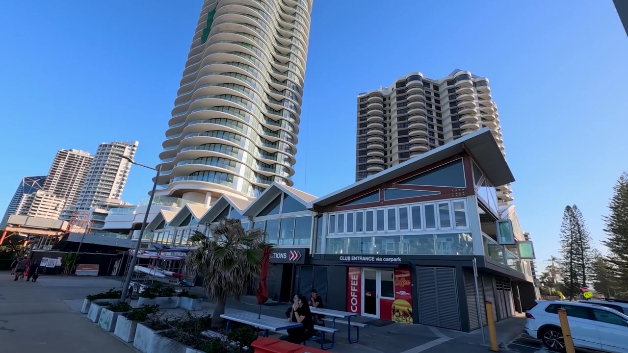 Paseo peatonal junto a rascacielos frente a la playa y una obra en construcción.