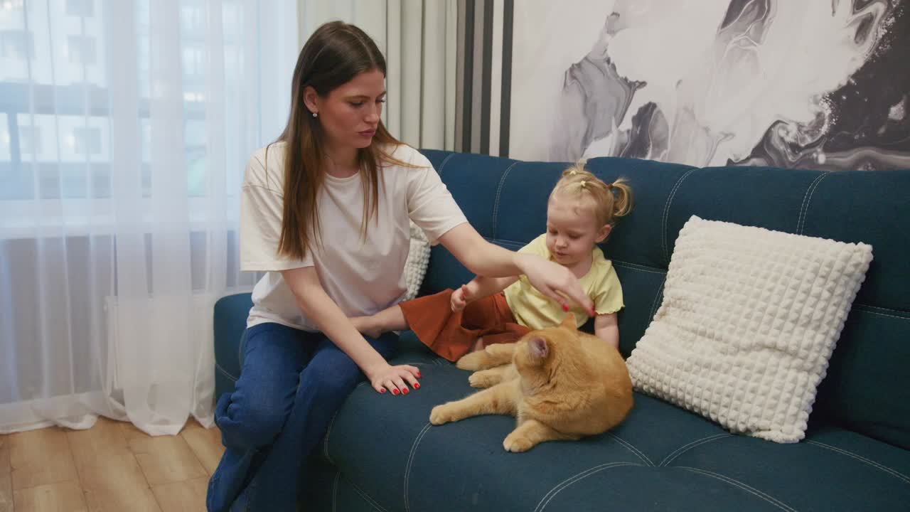Mor og barn klapper en oransje katt på en sofa