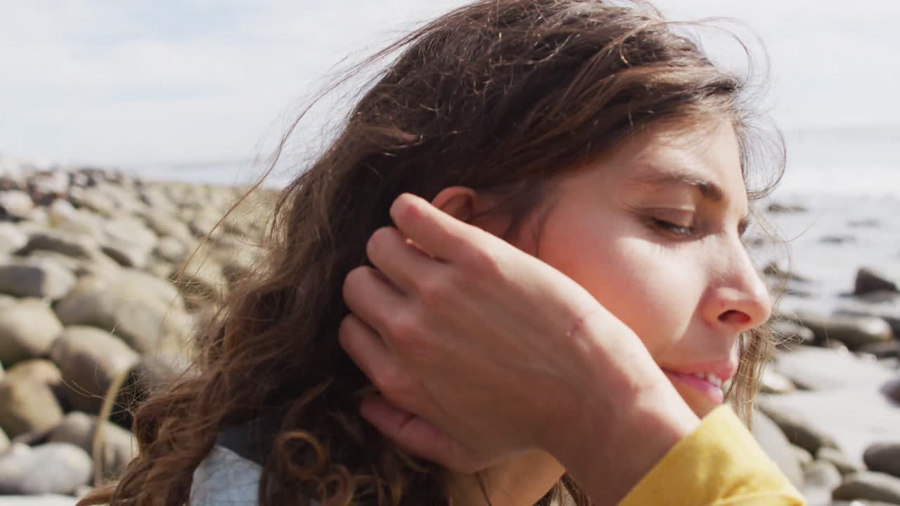 mujer de raza mixta pensativa sentada en la playa junto al mar, disfrutando de la vista y sonriendo