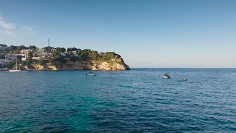 Fliegen-über-Der-Türkisfarbenen-Wasserbucht-Mit-Schwimmenden-Booten,-Sommer-Auf-Mallorca