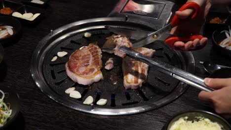 samgyeopsal - persona cortando panceta de cerdo a la parrilla con tijeras sobre una parrilla de carbón en un restaurante coreano