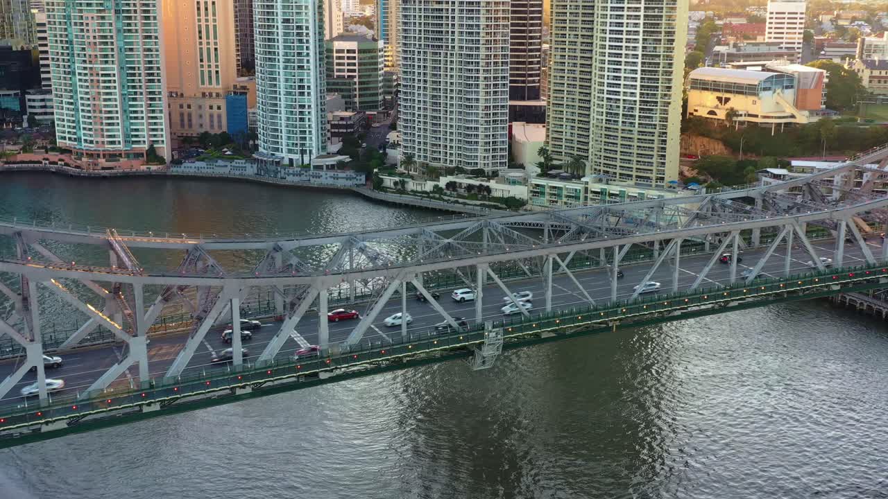 Aerial birds eye view, flyover Brisbane river along Story bridge capturing vehicle traffics travelling between Fortitude Valley and Kangaroo points with riverside downtown cityscape views at sunset