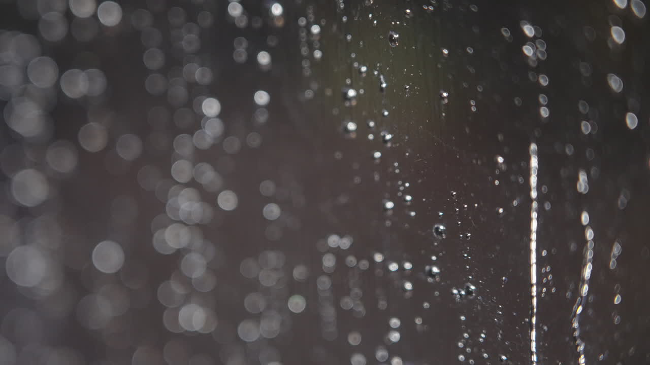 抽象的なボケ背景と窓に付いた雨粒のクローズアップ
