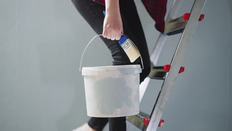 woman goes up step ladder holding paint brush and bucket