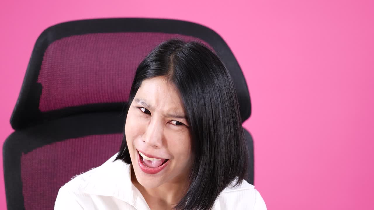 Smiling woman in white shirt laughs confidently, seated against pink background with bright lighting