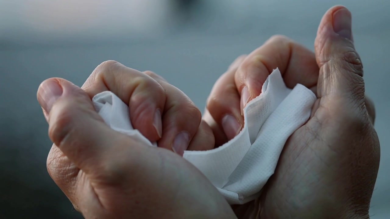 Presenting unfolded tissue, hands folding and crumpling napkin in tight closeup to form compact wad