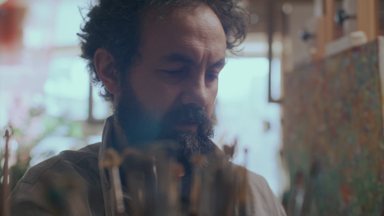 Focused Male Artist Choosing Paint Brushes in Creative Studio