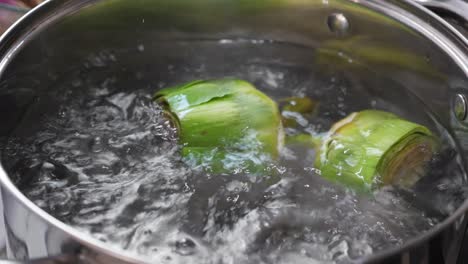 put and cooking artichokes in saucepan, closeup in the kitchen