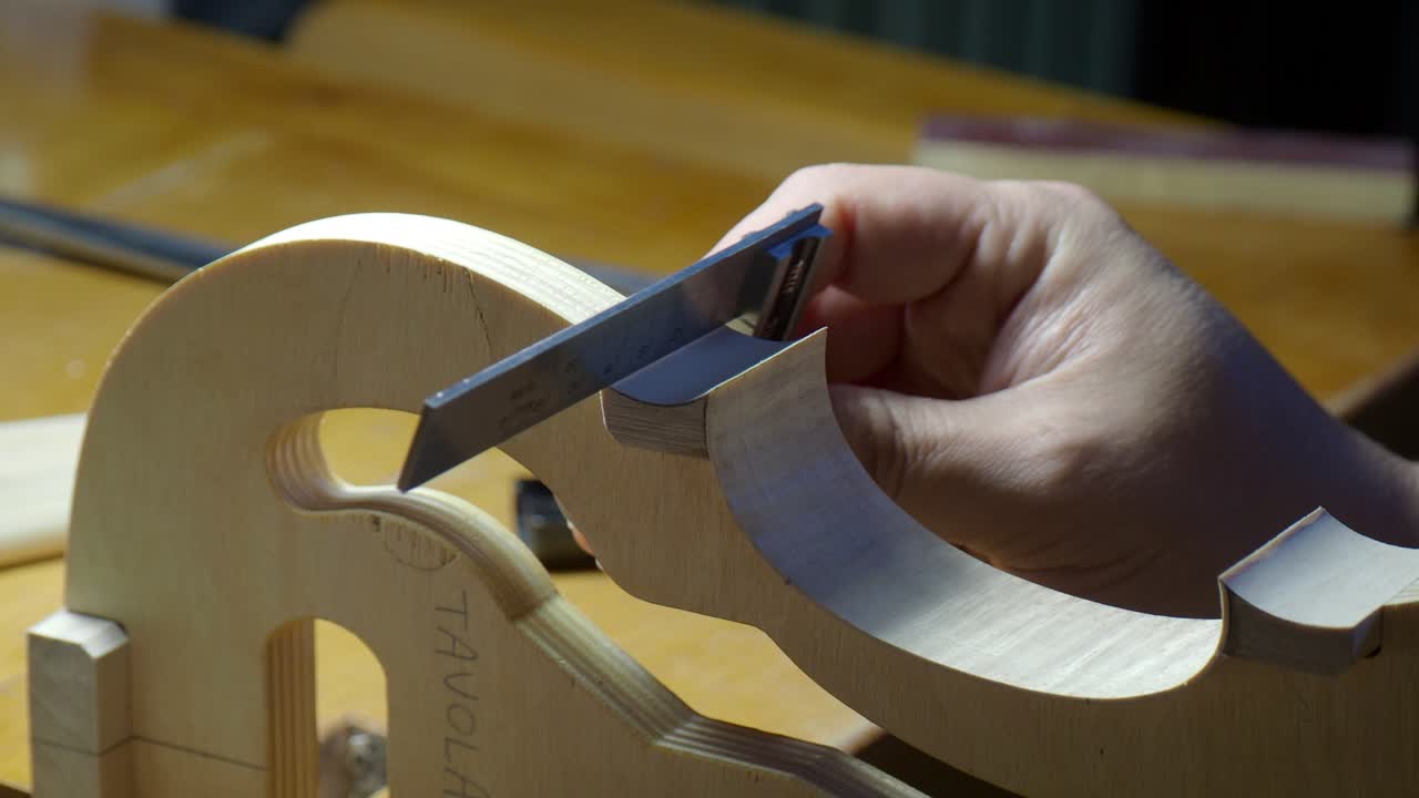 Violin rib and edge being refined with sandpaper by luthier hand on internal mold, smoothing curve and outline during traditional string instrument construction in workshop, close up handheld shot