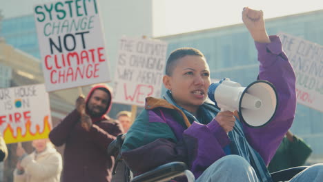 female protestor in wheelchair with placard and megaphone on demonstration against climate change