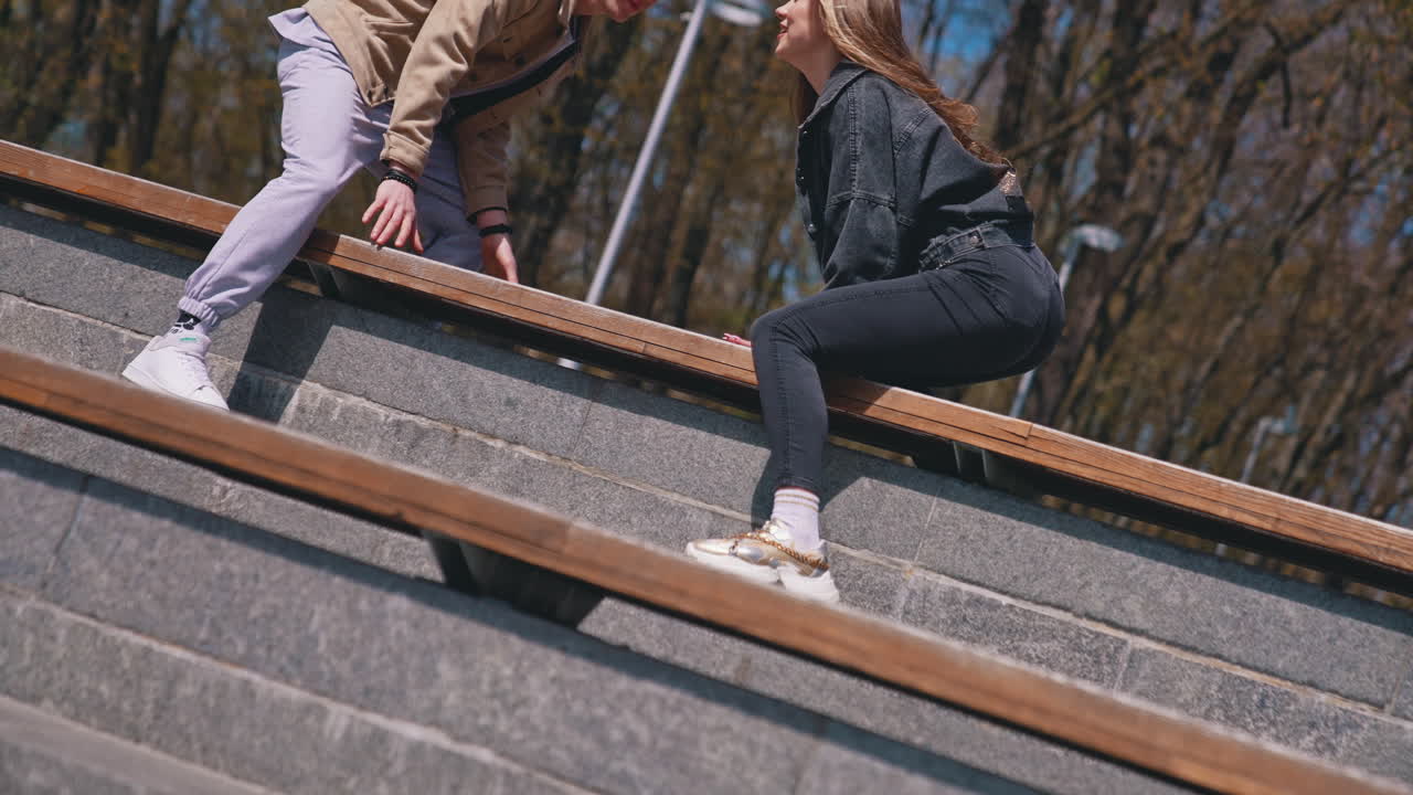 Happy couple sitting at the bench at the park. Good looking couple spending time with each other in the street in a sunny day. Young people enjoying the time together concept