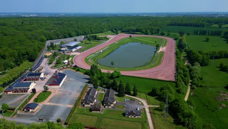 the drone pulls back from the laval racecourse, revealing surrounding forests, buildings, and a bird flying across the frame