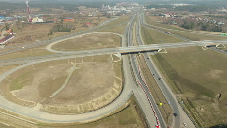 Elevated-roads-intersecting-over-flat-terrain,-with-traffic-circulating-amidst-construction-areas-and-nearby-urban-development