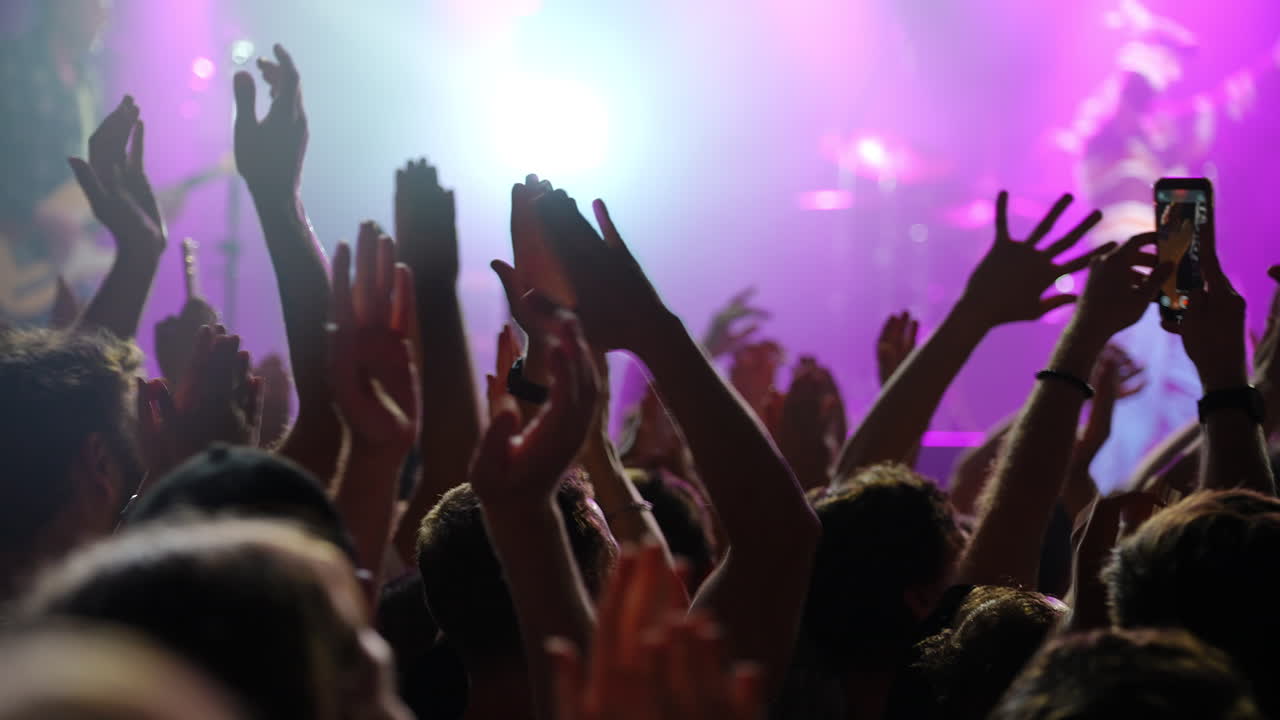 Folla di entusiasti partecipanti al concerto che alzano le mani con eccitazione sotto vivaci luci del palco.