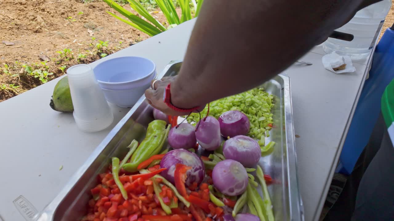 은 날씨에 을 잘라내는 기술로 야외의 금속 트레이에 은 고추, 양파, 녹색 고추, 토마토를 잘라내는 남자