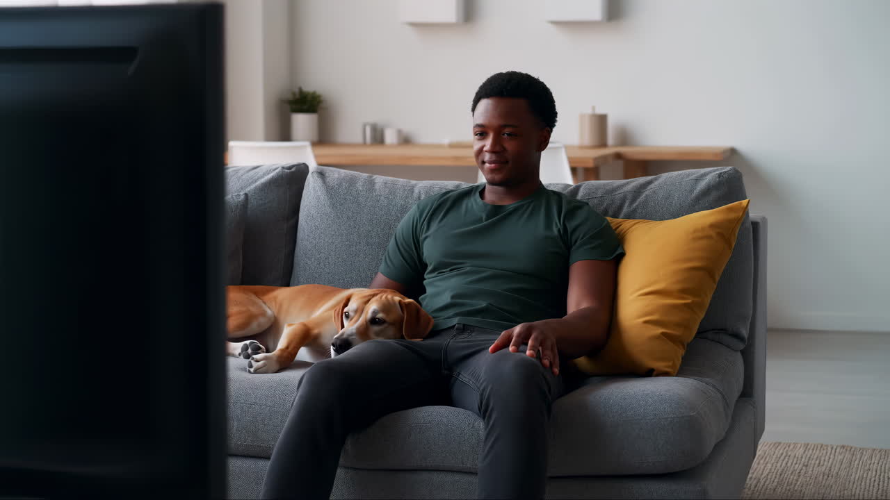 Junger Mann und Hund entspannen sich auf dem Sofa und schauen fern