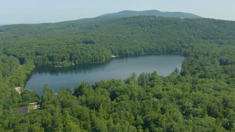 Tiro-Giratorio-De-Un-Dron-Aéreo-Sobre-El-Lago-Al-Atardecer-Rodeado-De-Un-Denso-Bosque-Verde-De-Coníferas-Sobre-Un-Terreno-Montañoso-Durante-El-Día