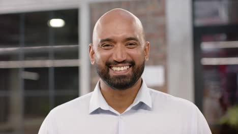 Portrait-of-happy-biracial-bald-creative-businessman-with-beard-smiling-in-office,-in-slow-motion