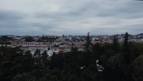revealing shot of the cloudy city of braga, portugal in the middle of a forest - drone shot